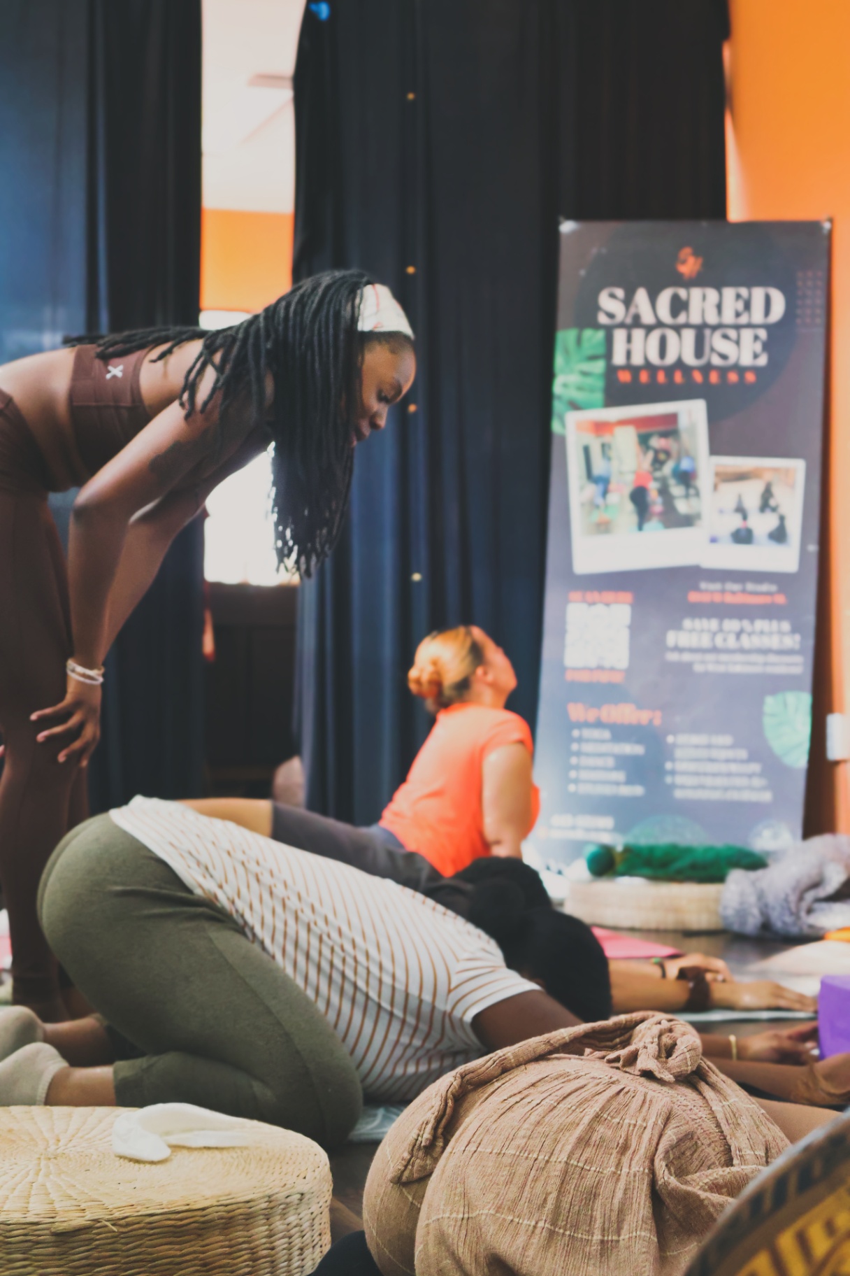 Empress Ka leading assisted stretch beside the Sacred House Wellness banner